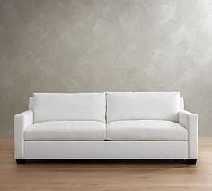 a white couch sitting on top of a hard wood floor next to a gray wall