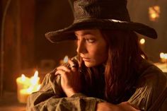 a woman wearing a hat and holding a cell phone to her ear while sitting in front of a fire