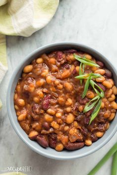 a bowl filled with beans and garbanzo on top of a table next to green onions