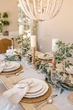 a dining room table set with place settings, candles and greenery on the tables