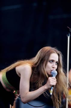 a woman with long hair holding a microphone in front of an audience at a music festival