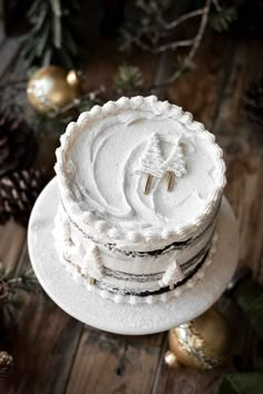 a white cake with frosting and decorations around it on a wooden table next to pine cones