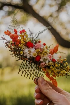 a person holding a comb with flowers on it in front of some grass and trees