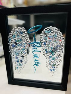 an image of two wings made out of beads on display in a black frame with blue ribbon