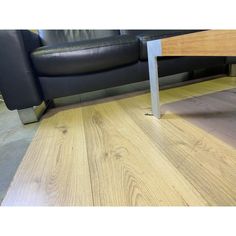 a black leather couch sitting next to a wooden table on top of a hard wood floor