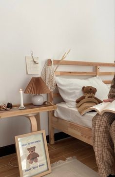 a person sitting on a bed reading a book with a teddy bear next to them