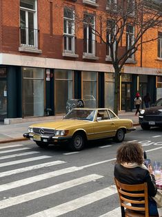 two people sitting at a table in front of a yellow car on the side of the road