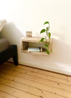 a small shelf with some books and a potted plant on it next to a bed