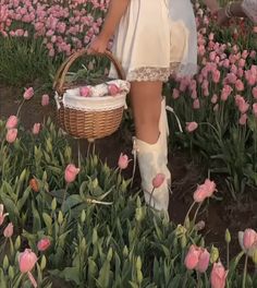 a woman in a white dress holding a basket and walking through a field full of pink tulips