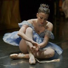 a young ballerina is sitting on the floor tying her ballet shoes with one hand