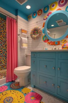 a colorful bathroom with blue cabinets and pink shower curtain, rugs on the floor