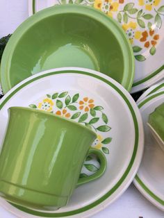 a green cup and saucer sitting on top of plates with flowers painted on them