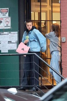 two people standing outside of a building with signs on the door and one person holding a drink