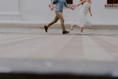 a man and woman holding hands while walking down the street in front of a building