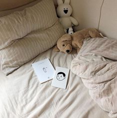 two stuffed animals sitting on top of a bed next to an open book and pillow