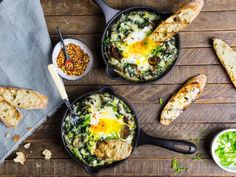 three skillets filled with different types of food on top of a wooden table next to bread