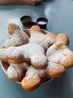 powdered sugar coated donuts in a bowl with dipping sauces on the side