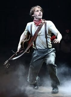 a man holding a guitar in his right hand and wearing suspenders on the other