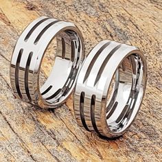 two wedding bands with black and white stripes on them sitting on top of a wooden surface