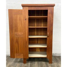 a wooden bookcase with shelves and doors on the front, against a white brick wall