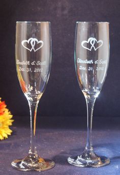 two wine glasses with hearts on them sitting next to a vase and yellow flower in the background