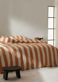 an orange and white striped bed spread in a room with a bench next to it