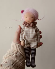 a hand holding a small doll with pink hair