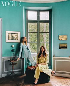 two women are sitting on suitcases in a room with blue walls and wood floors