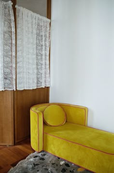 a yellow couch sitting in front of a window next to a white rug on top of a hard wood floor