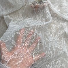 a person's hand is seen through the net on a white cloth with small flowers