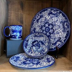 blue and white plates are stacked on top of each other in a wooden box with two mugs next to it