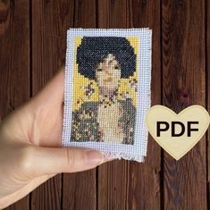 a hand holding up a small cross stitch picture with the image of a woman's face on it