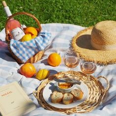 a picnic with bread, oranges and wine on a blanket in the grass next to an open book