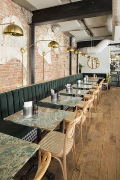 tables and chairs are lined up against the brick wall in this dining room with green velvet booths