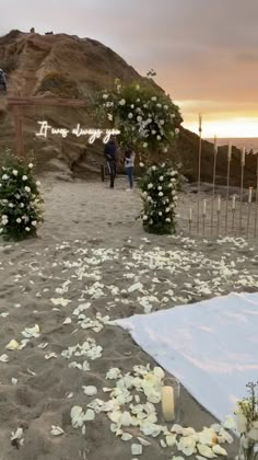 an outdoor wedding setup with flowers and candles on the ground at sunset, in front of a large rock outcropping