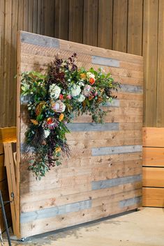 a wooden wall with flowers hanging from it's sides and another piece of wood behind it