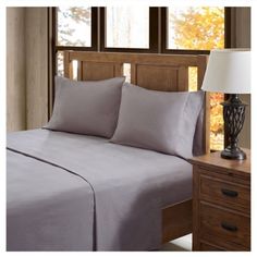 an image of a bed with grey sheets and pillowcases in the bedroom setting