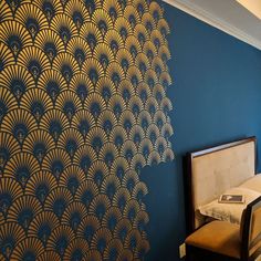 a bed sitting next to a blue wall with gold designs on the wall and a chair in front of it