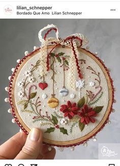 a hand holding a small embroidered ornament with red and white flowers on it