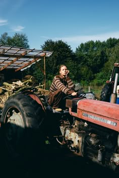 a woman sitting on the back of a red tractor next to a pile of wood