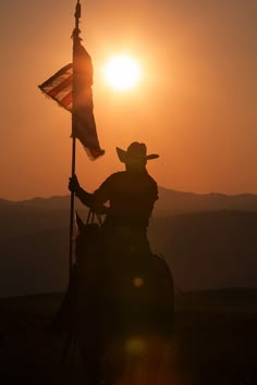 a man riding on the back of a horse next to a american flag at sunset