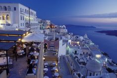 an outdoor dining area overlooking the ocean at dusk with people eating and drinking on tables