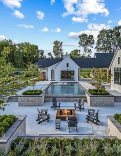 an outdoor fire pit surrounded by chairs and tables in front of a white house with a pool