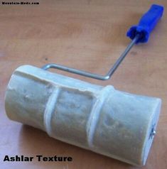 a close up of a paint roller on a wooden surface with a blue brush in the background