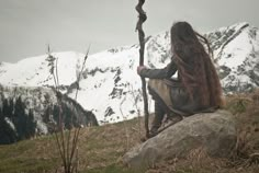 a woman with long hair sitting on top of a rock