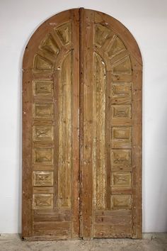 two wooden doors with arched top and bottom panels on each side, in front of a white wall