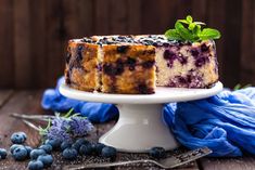 a blueberry cheesecake on a white cake plate with fresh blueberries around it