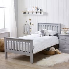 a white bed sitting in a bedroom next to a dresser and window on top of a hard wood floor