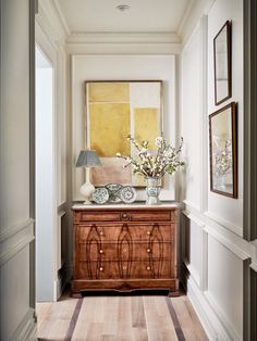 a wooden dresser sitting next to a wall with pictures on the wall and flowers in vases