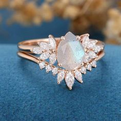 an opal and diamond ring on top of a blue surface with flowers in the background